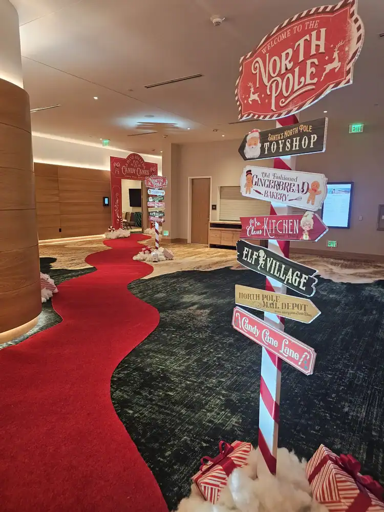 Festive holiday signs and red carpet in a decorated indoor space.
