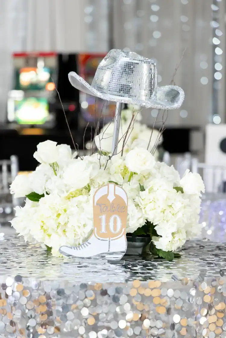 White floral centerpiece with silver cowboy hat for celebration decor.