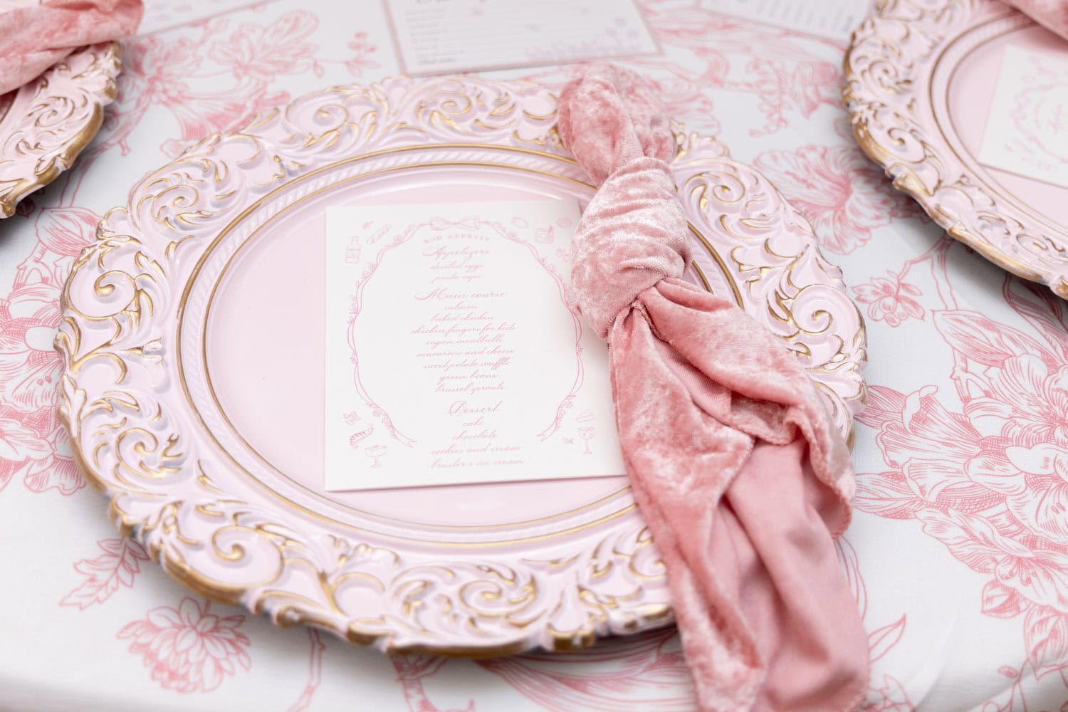 Elegant pink and gold table setting with ornate plates and pink velvet napkin.