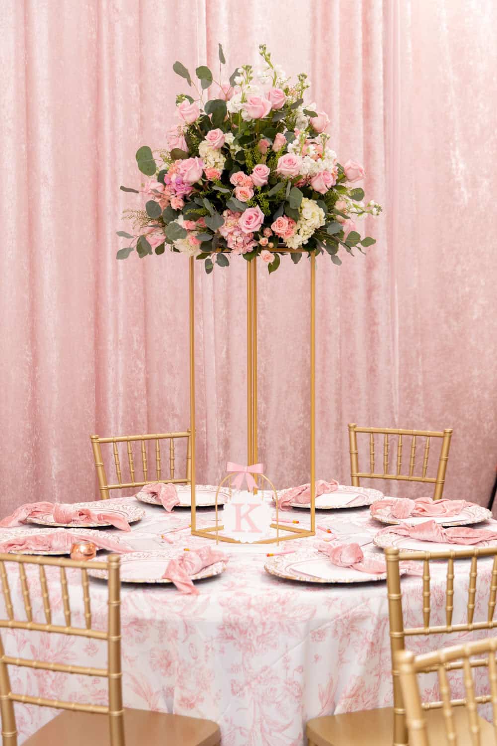 Pink floral centerpiece on a gold stand for event decor.