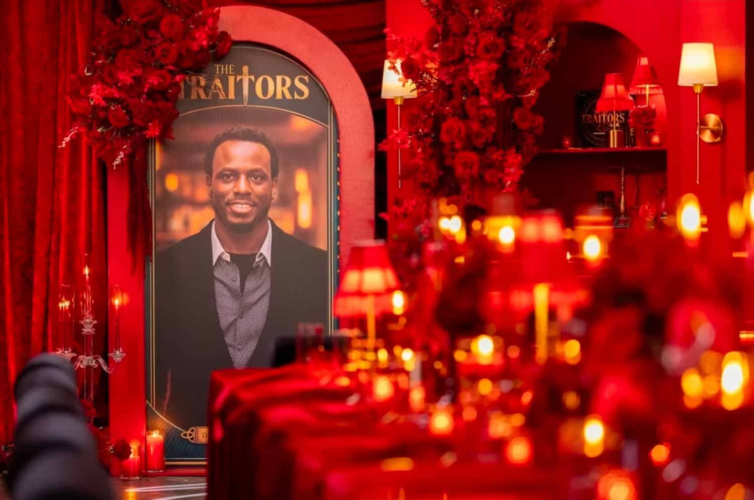 Portrait of a man at The Traitors event with red decor and candles.