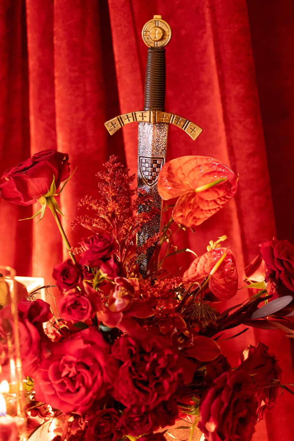 Decorative sword embedded in a floral arrangement with red flowers and red curtains.