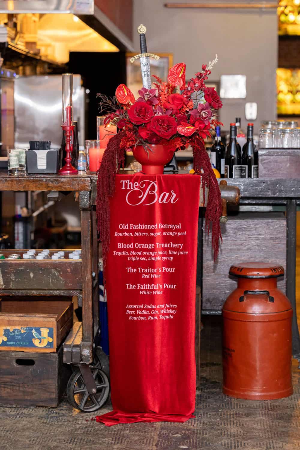 Red floral arrangement at a bar with wine bottles and candles.