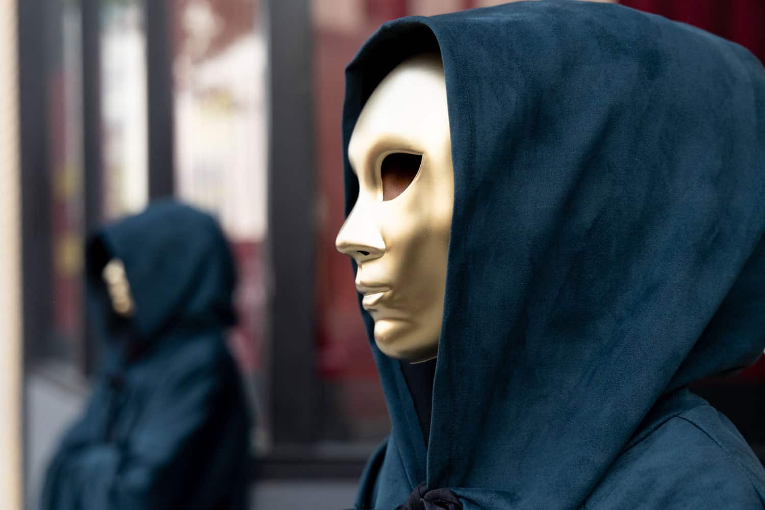 Person wearing a hoodie and mask, looking to the side, urban background.
