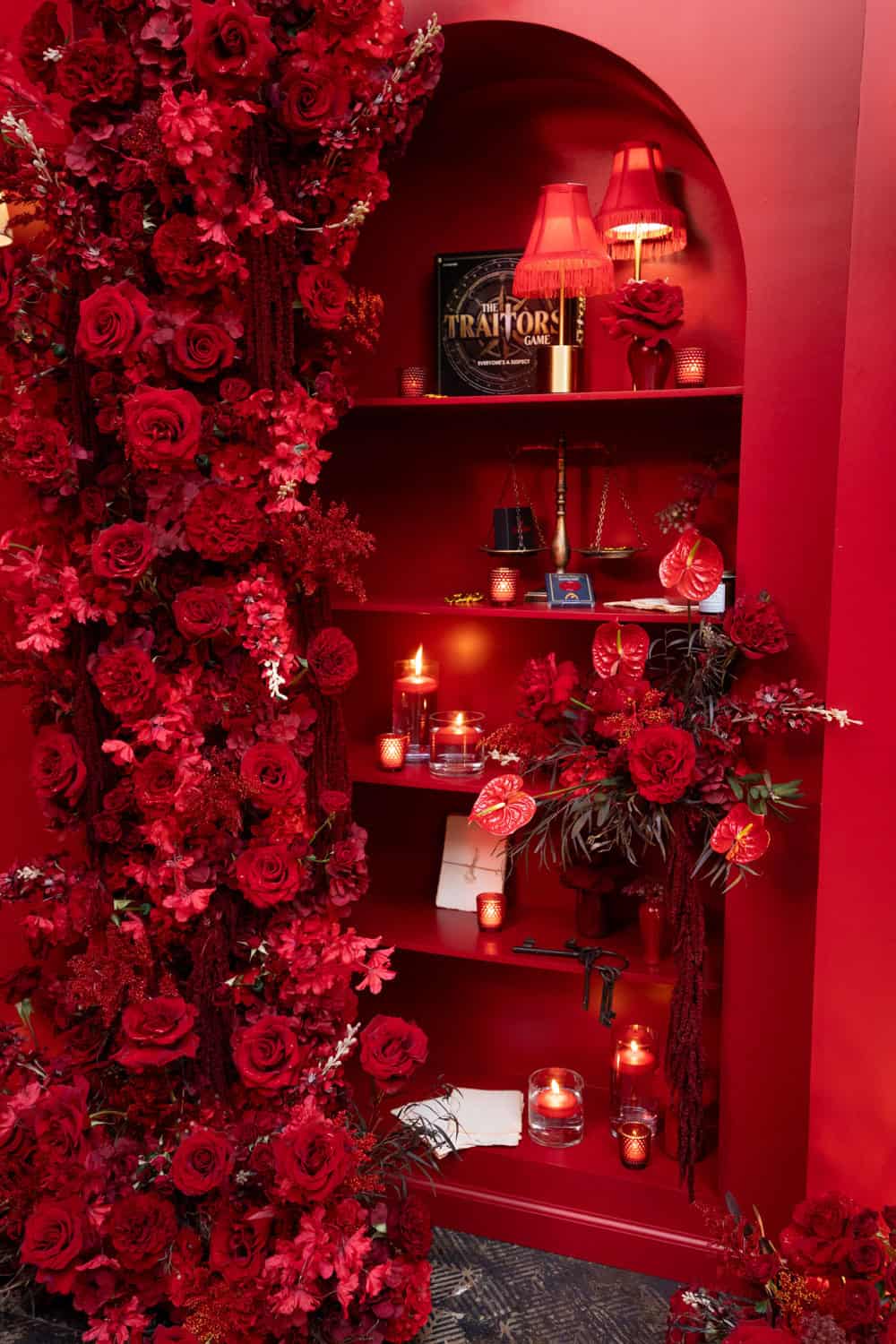 Red floral arrangement with candles and decorative items in a niche.
