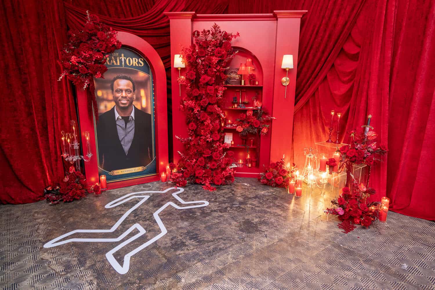 Red event decor with floral arrangements and a portrait of a man in a suit.