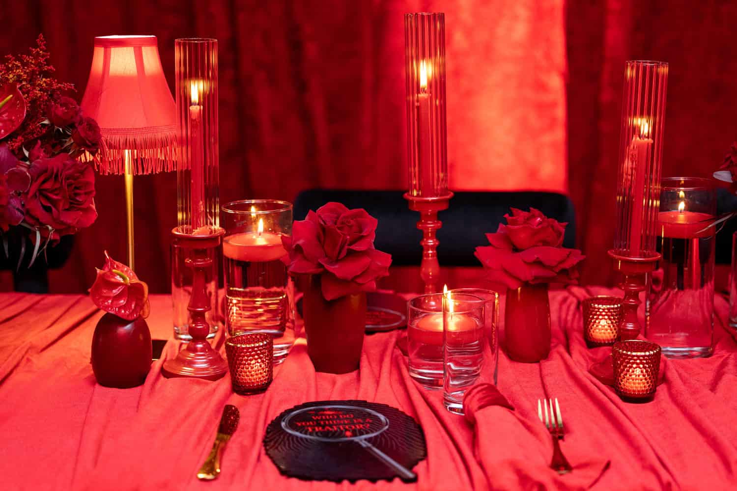 Red-themed table setting with candles, flowers, and glassware for a special event.