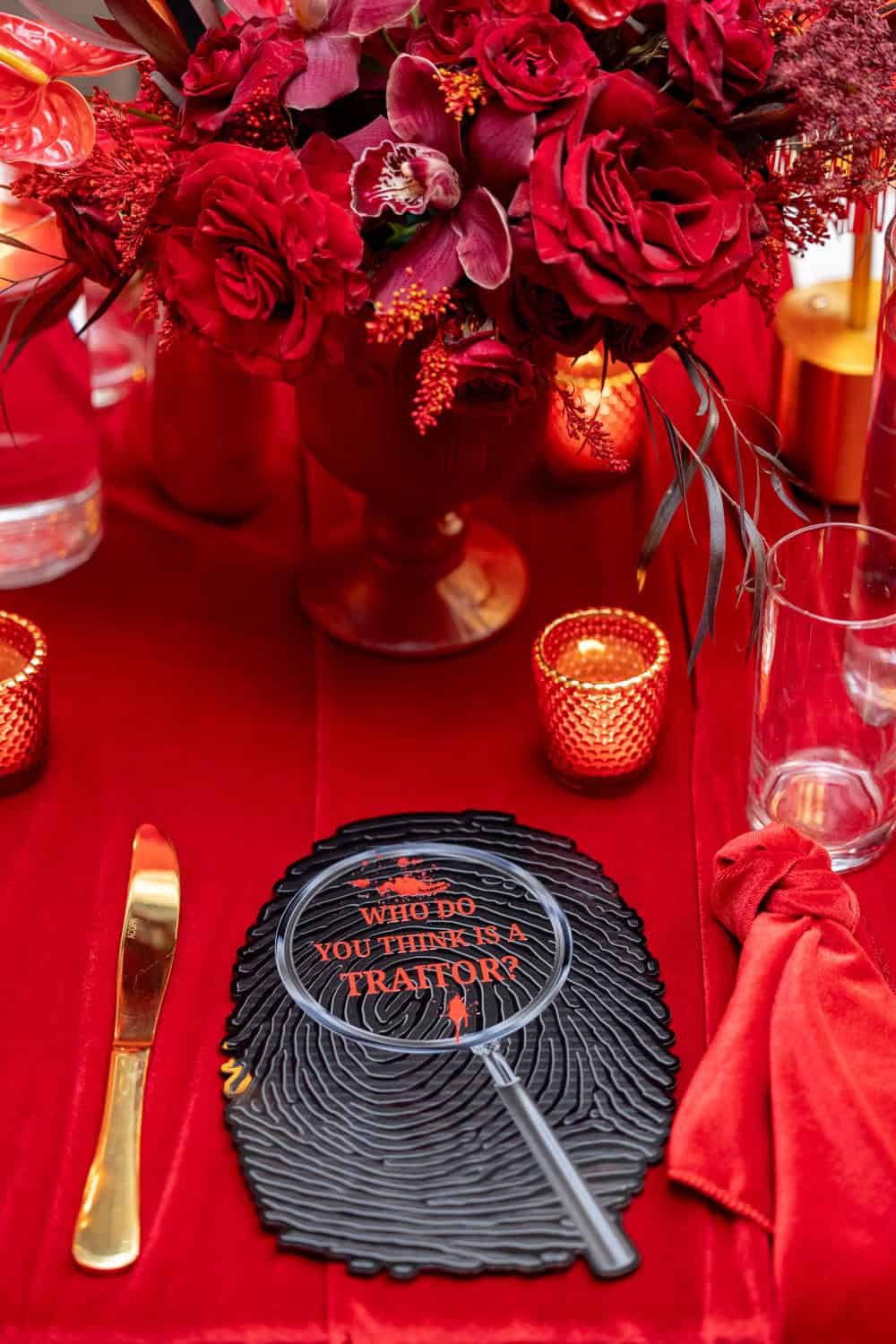 Red floral centerpiece with candles and table setting for event.