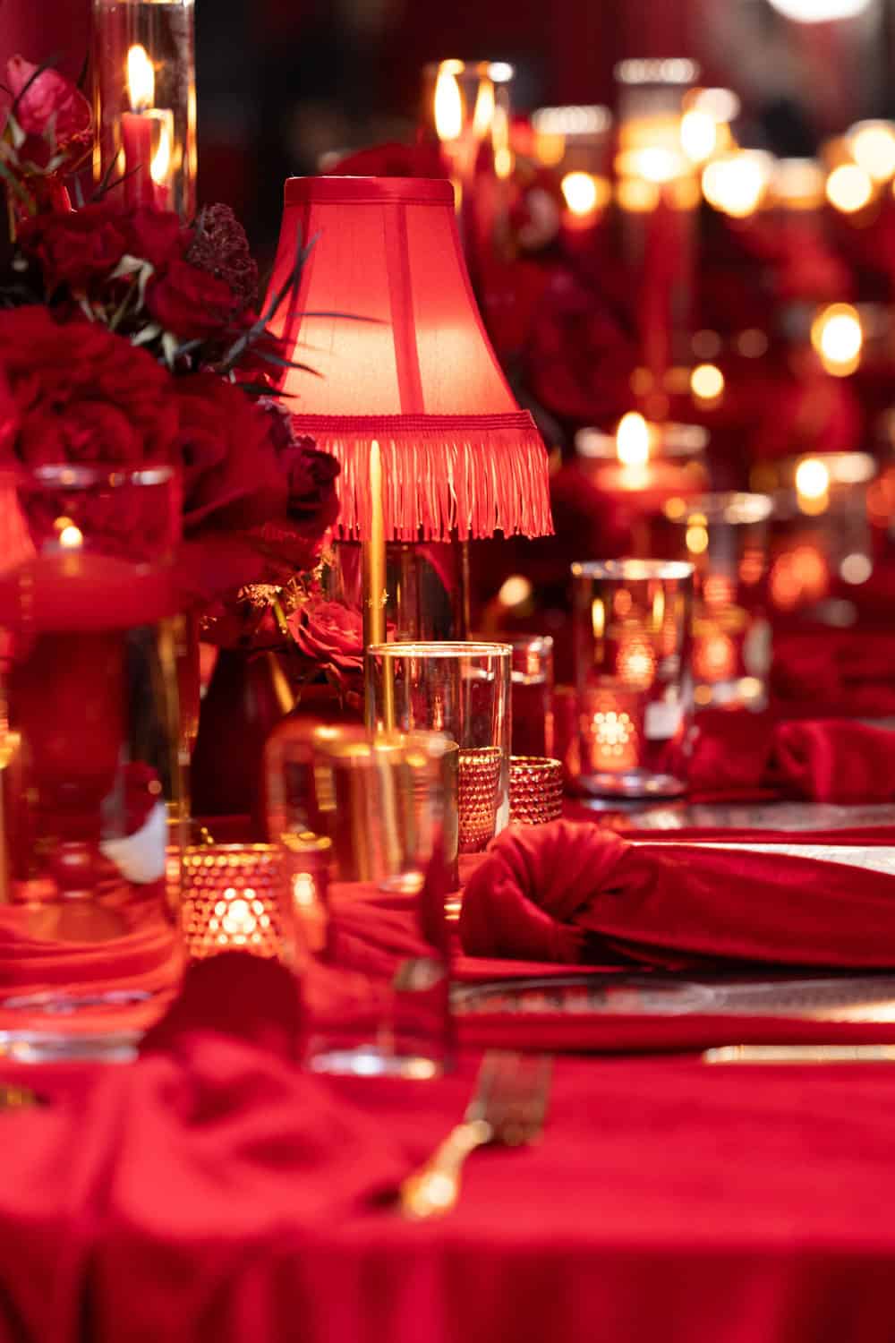 Red table setting with candles, flowers, and a lamp for a sophisticated event.
