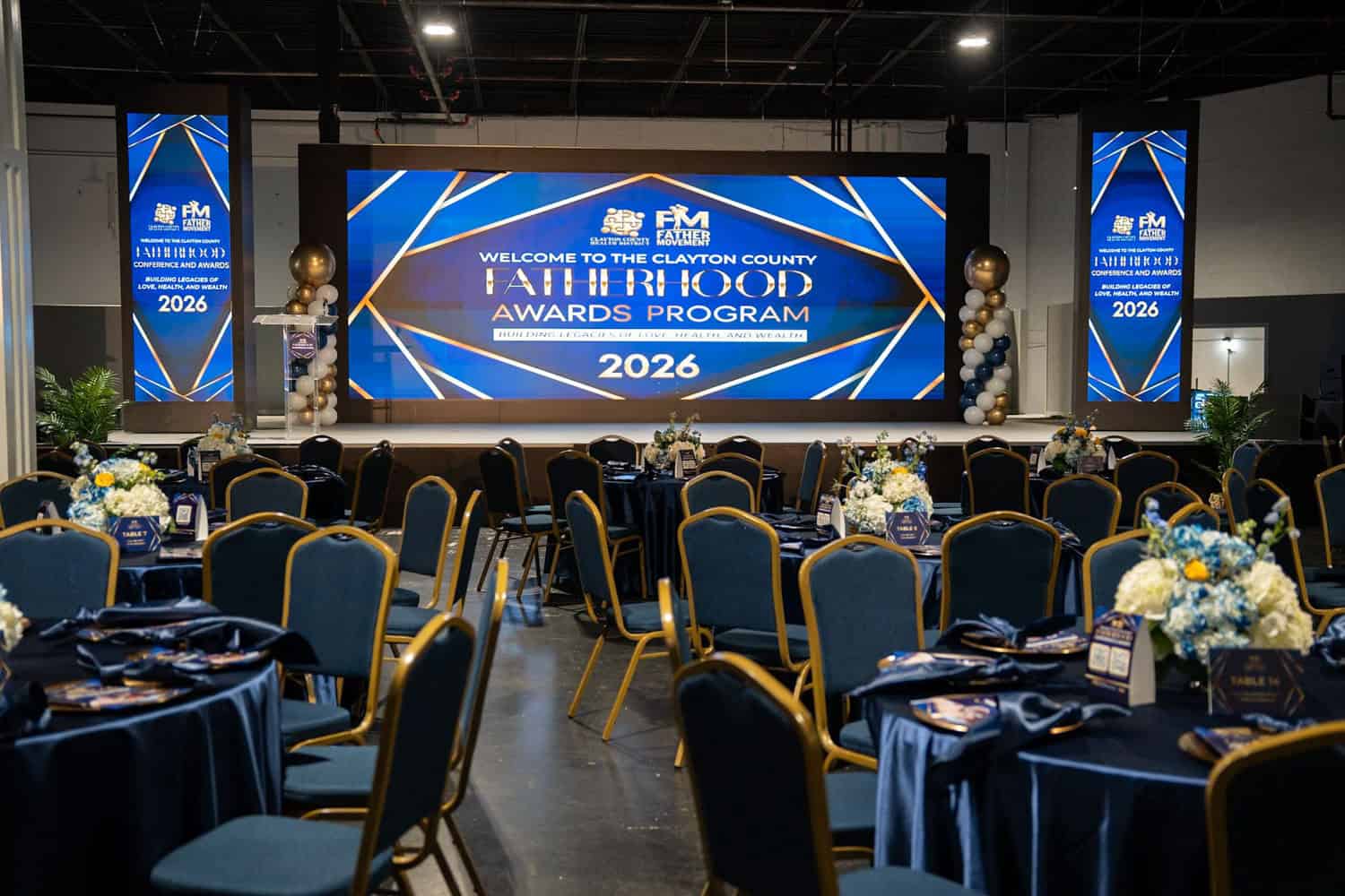 Event setup with stage, large screen, and decorated tables for awards ceremony.