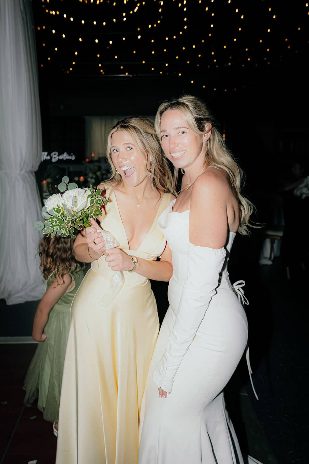 Two women smiling at a formal event, holding a bouquet of flowers.