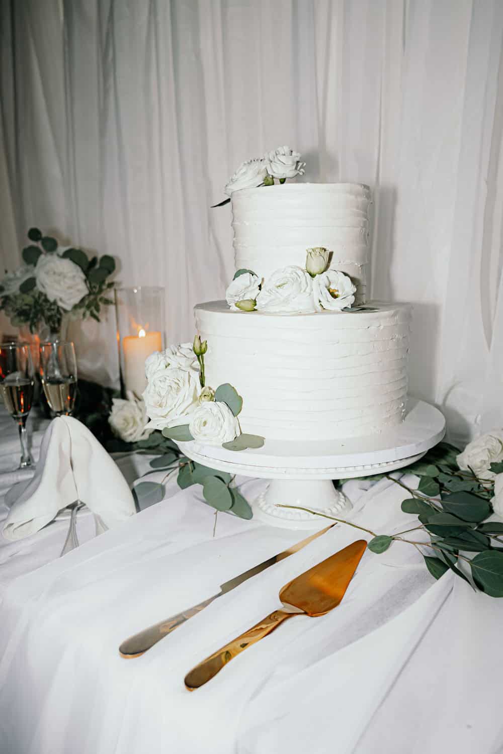 Two-tier white wedding cake with floral decorations and greenery.