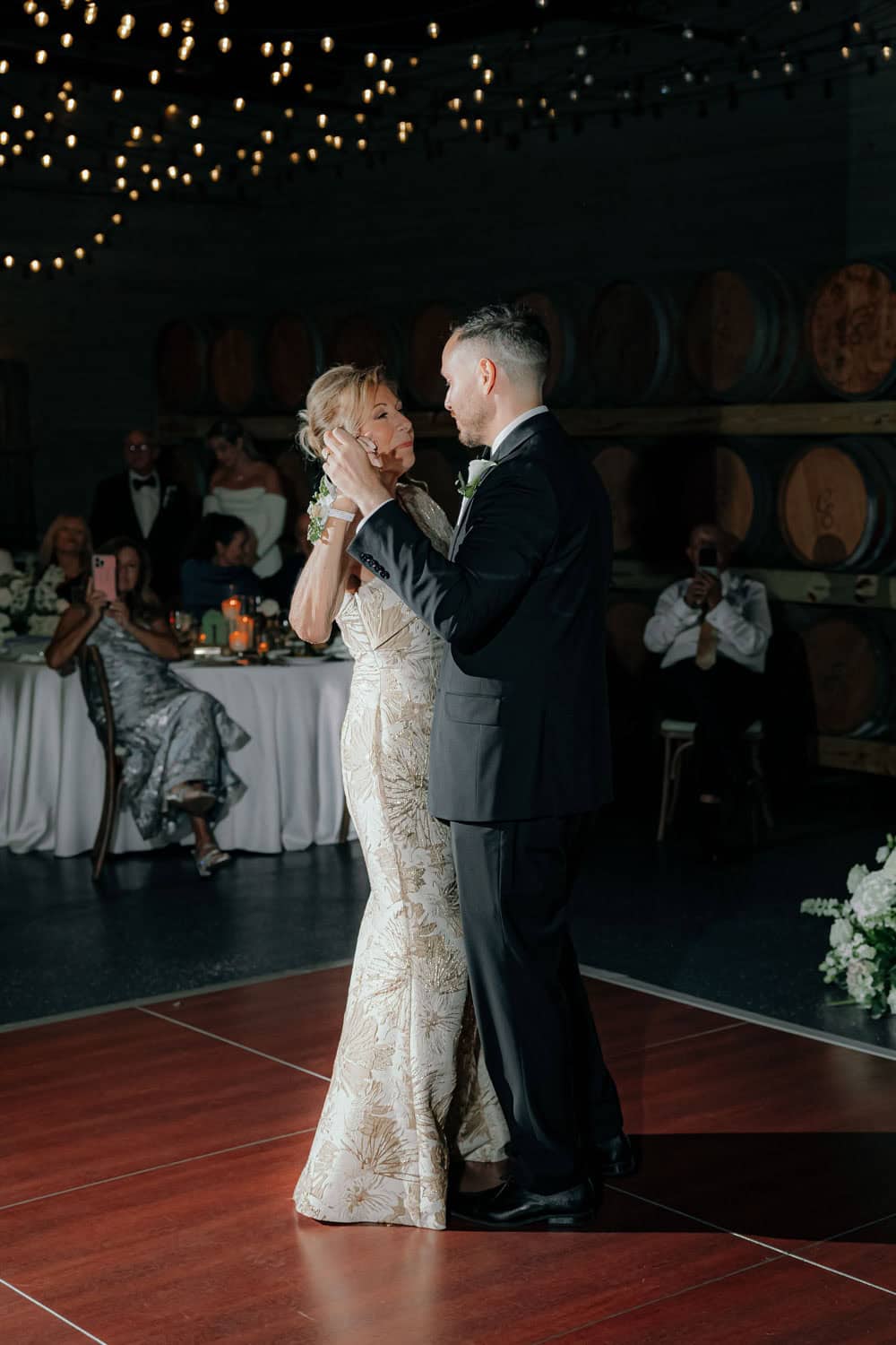 Bride and groom dancing at wedding reception with guests in background.