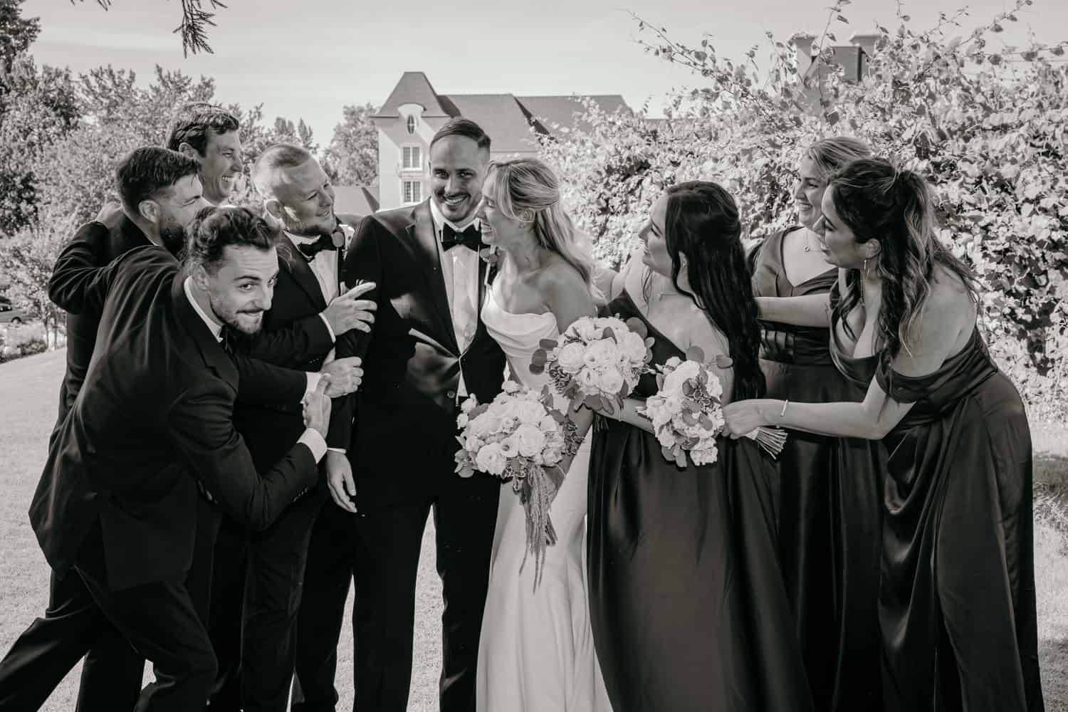 Joyful wedding scene with bride, groom, and friends outdoors.