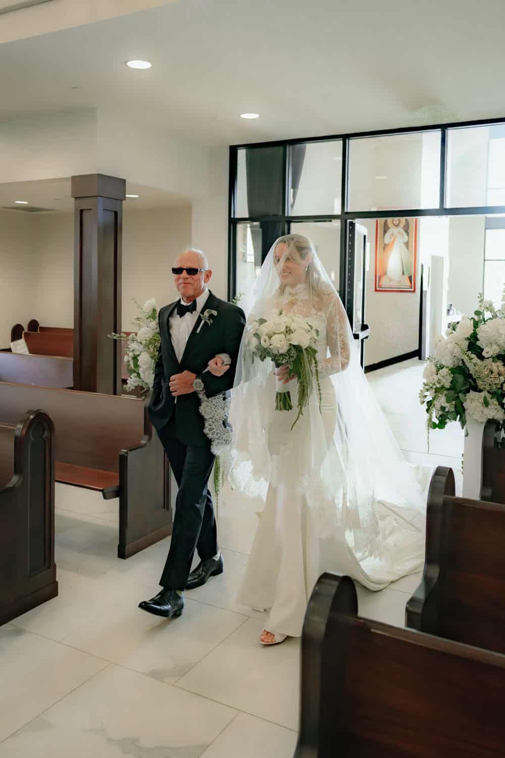 Bride in wedding dress walking with escort in church setting.
