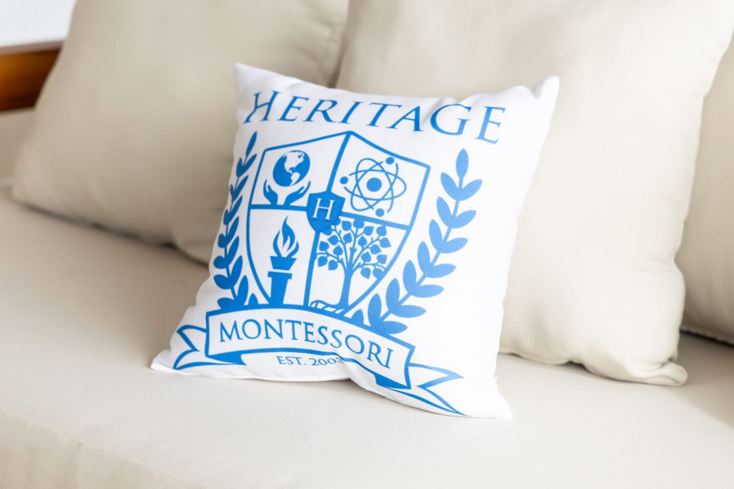 Heritage Montessori school pillow with emblem on a white couch.