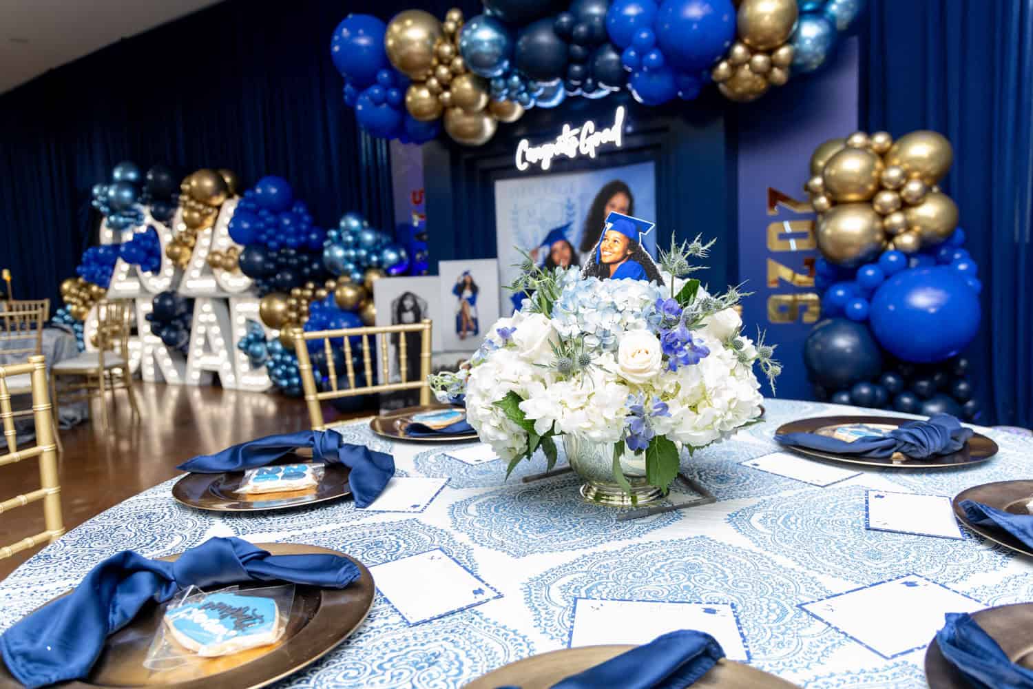 Graduation celebration table with blue and gold balloons and floral centerpiece.