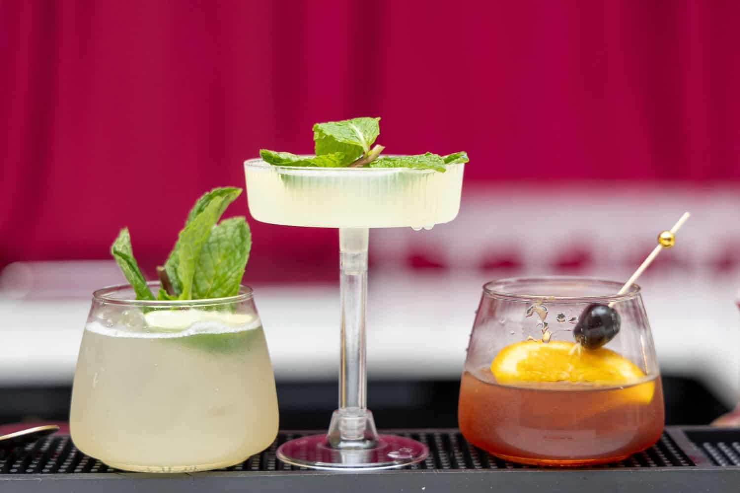 Three colorful cocktails with garnishes on a bar counter.